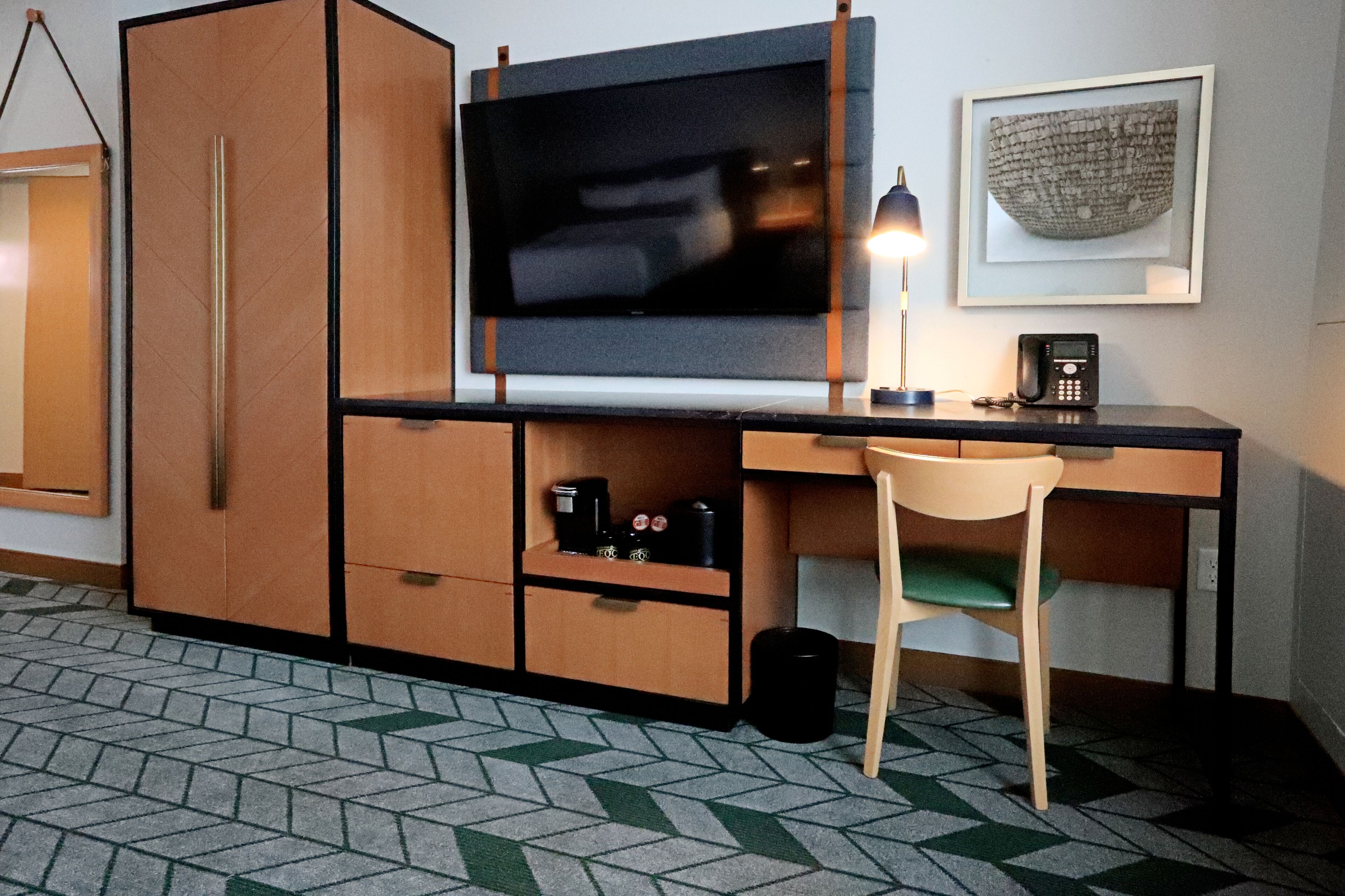 A compact room with a desk, chair, television, and a framed artwork on the wall.