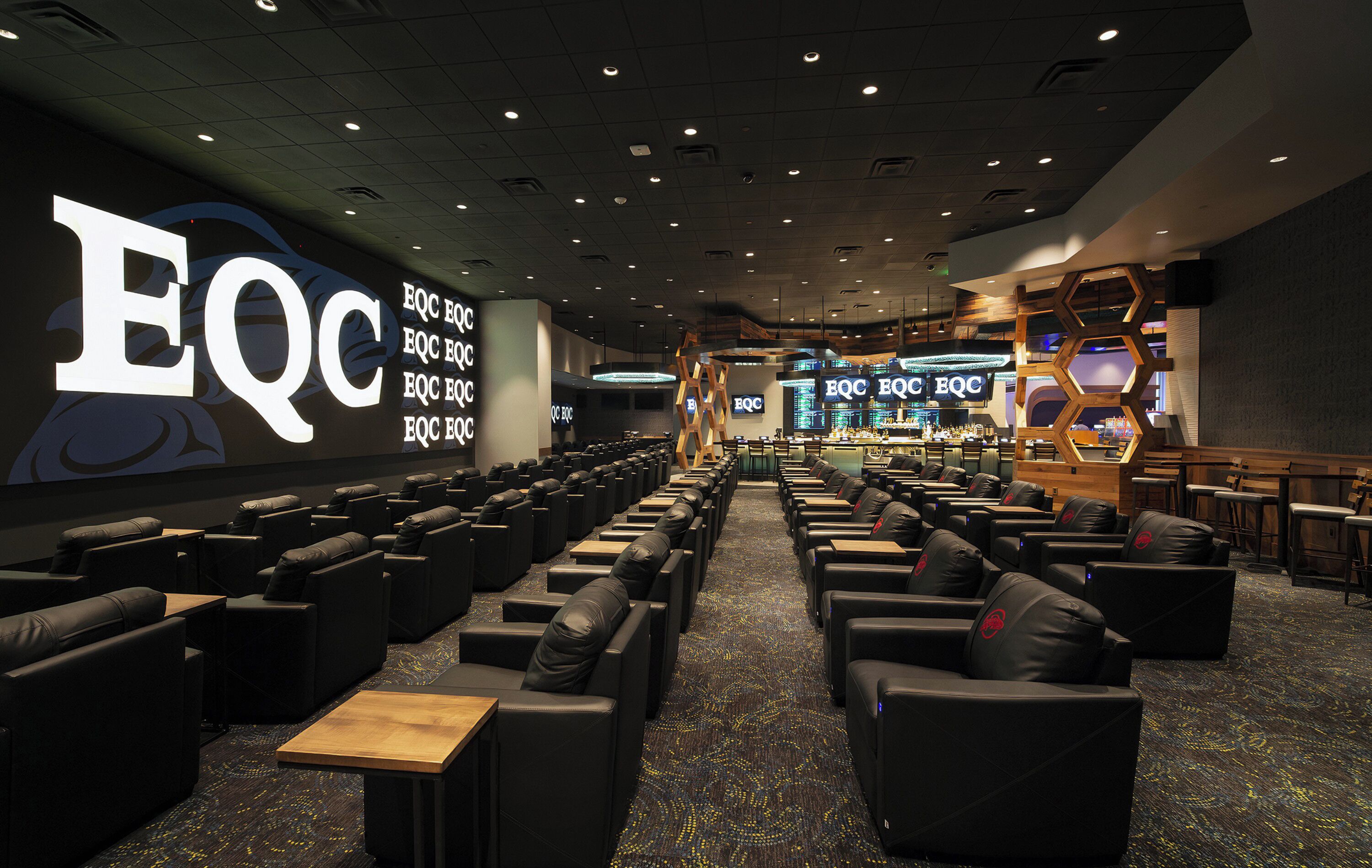 A cinema with rows of black leather seats and a large EQC logo on the wall.