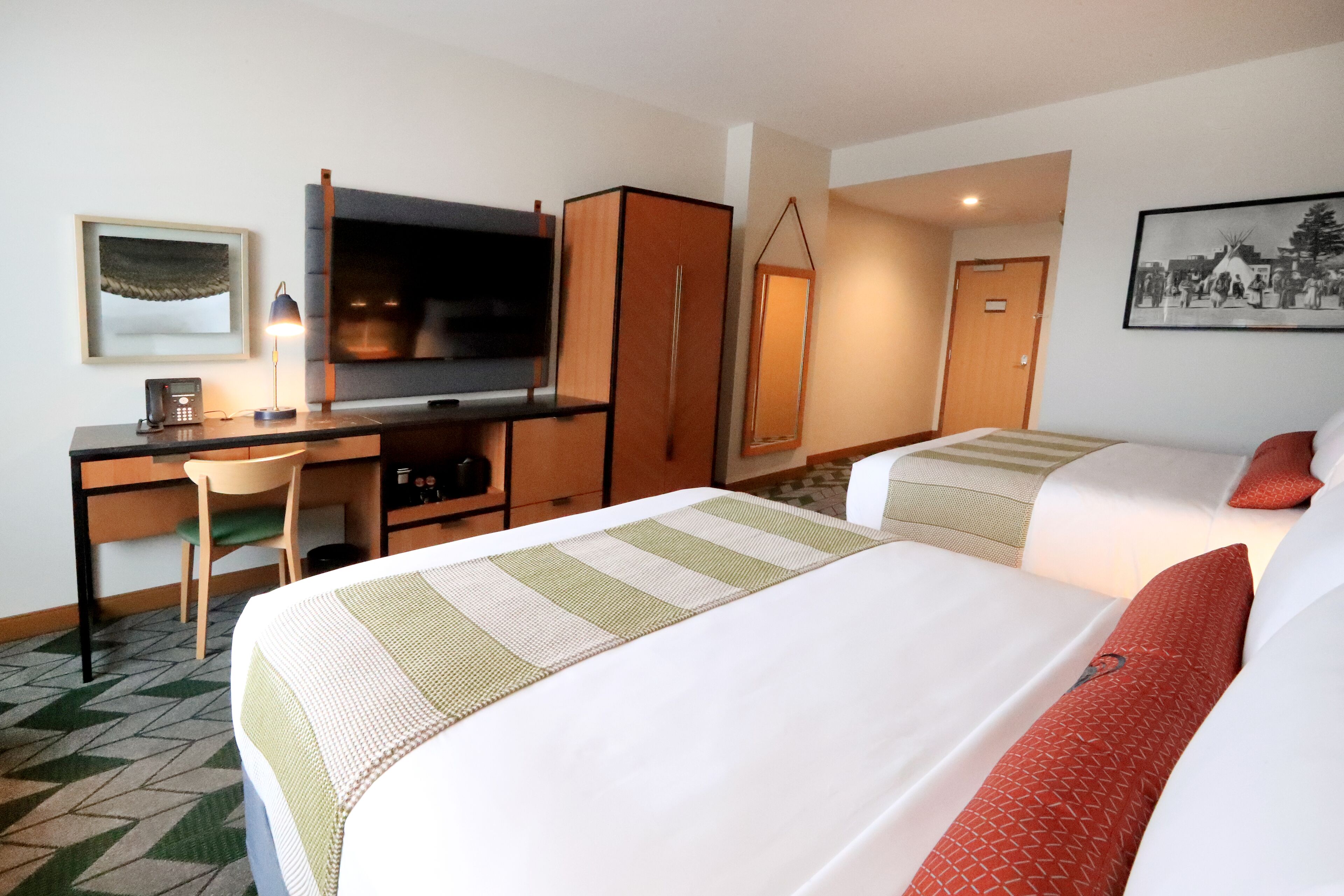 A hotel room with two beds, a desk with a chair, a television, and a framed picture on the wall.
