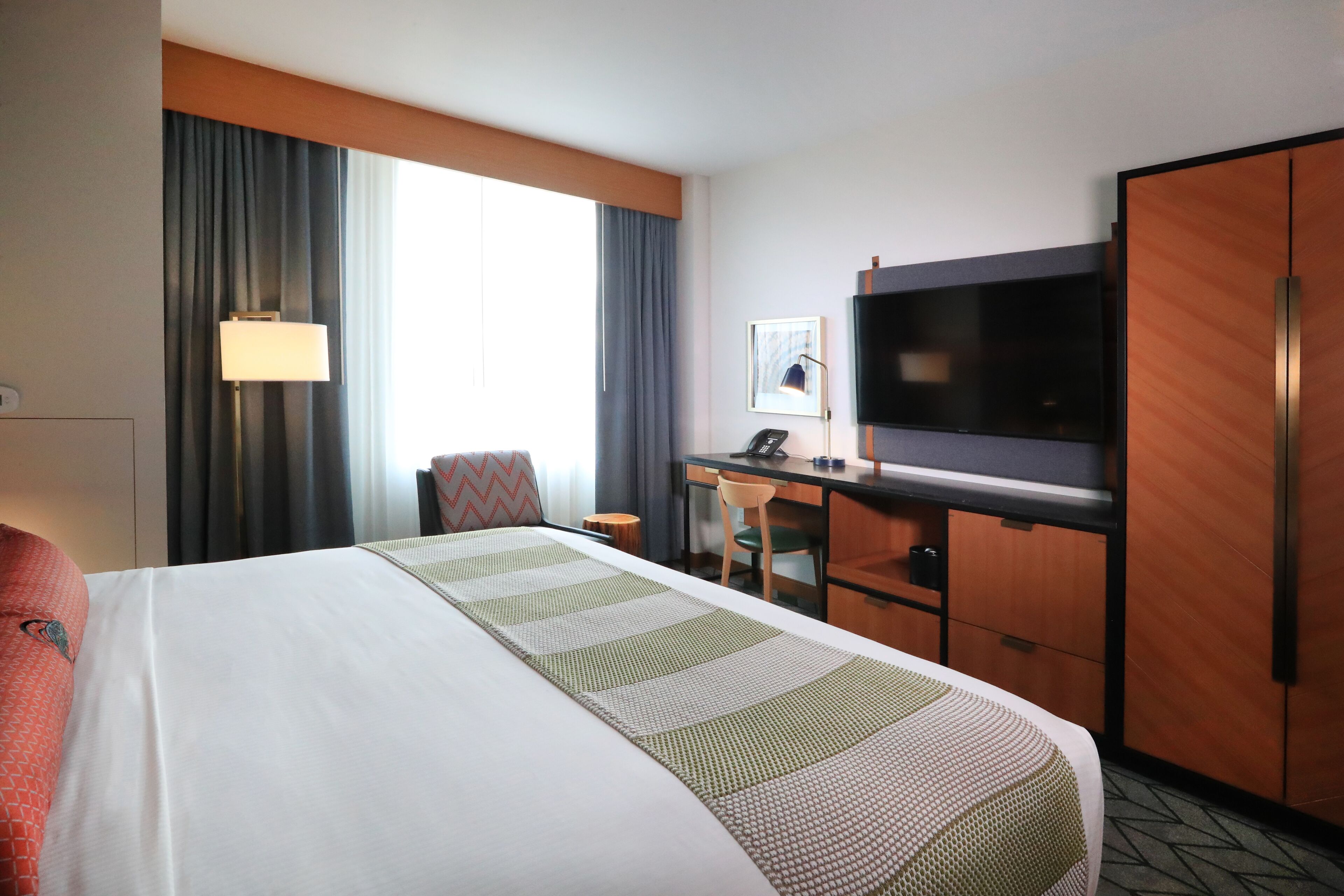A hotel room with a large bed, a desk with a chair, a television, and a wardrobe.