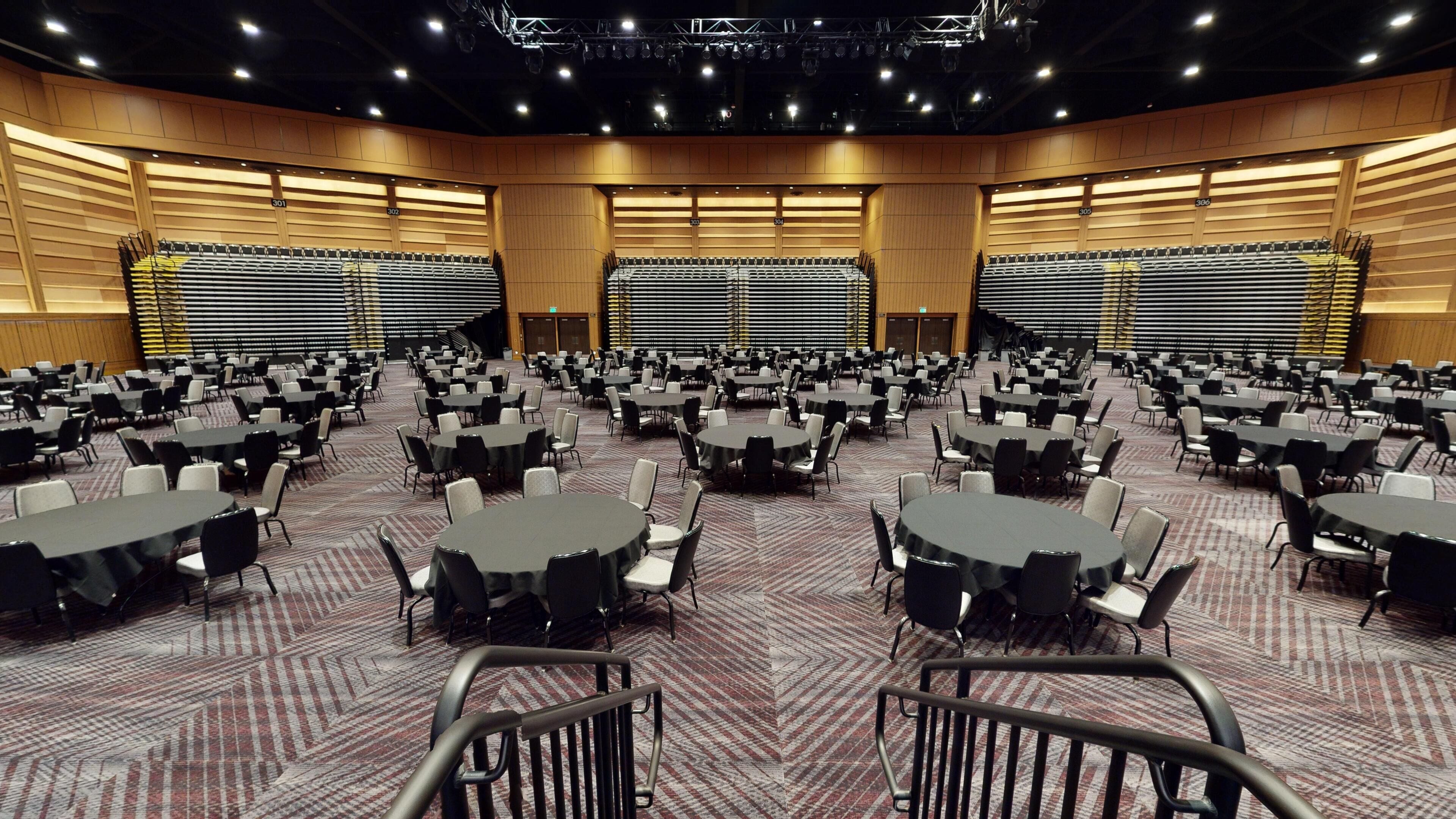 A large conference room with multiple round tables and chairs, arranged in rows.