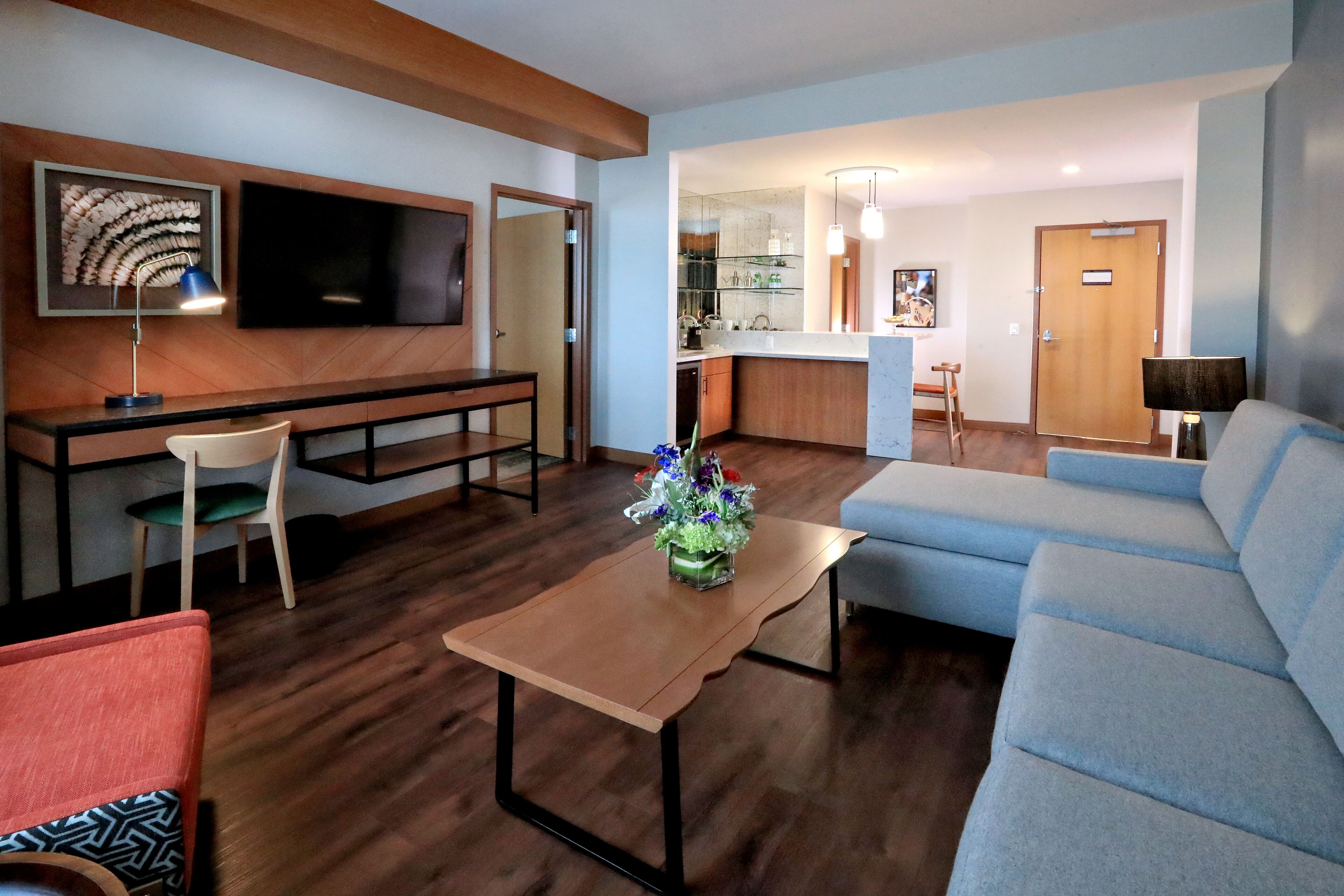 Una sala moderna con sofá, una mesa de centro, televisor, un comedor con sillas y una cocina al fondo.