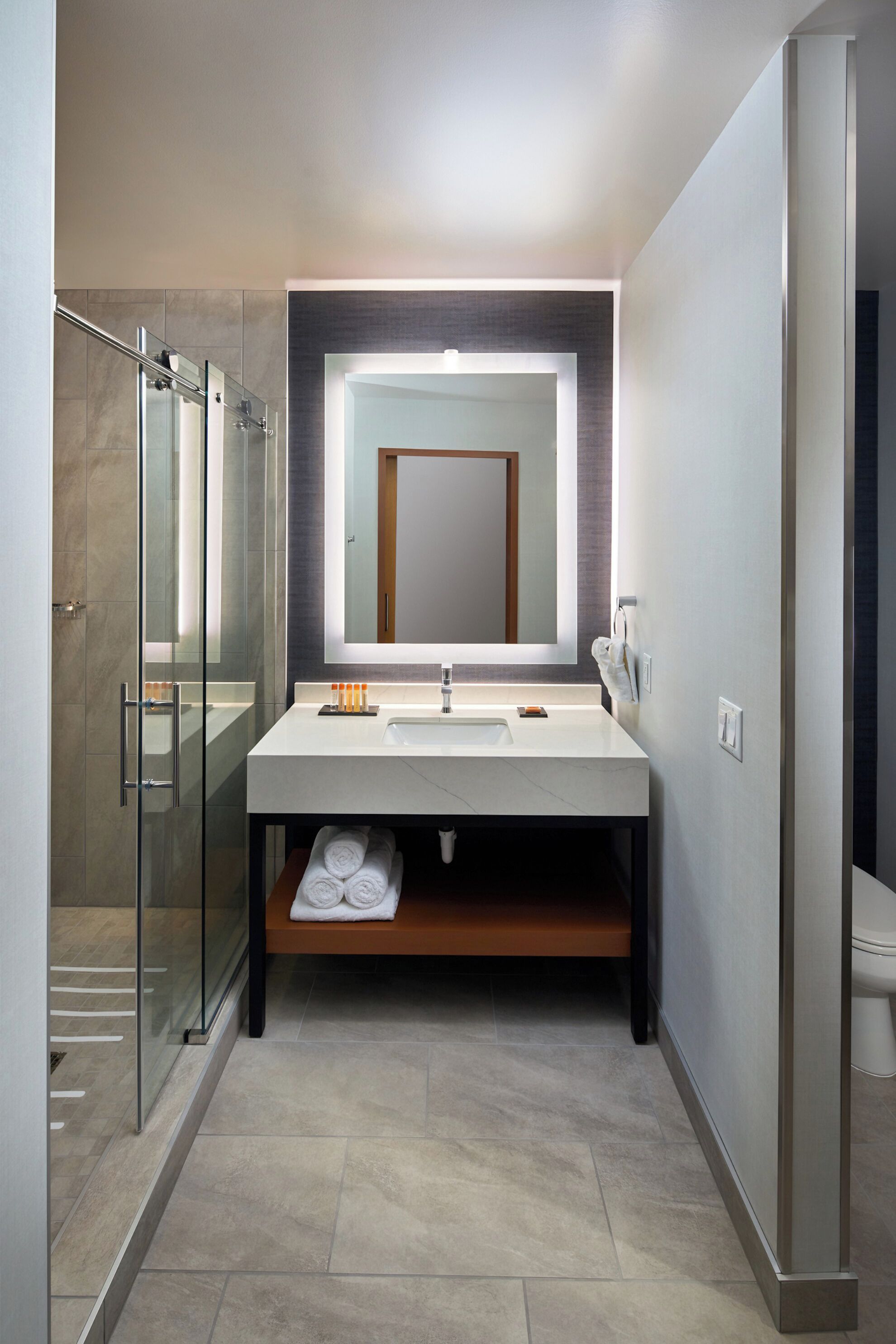 Un baño moderno con cabina de ducha de vidrio, un espejo grande y un lavabo blanco.
