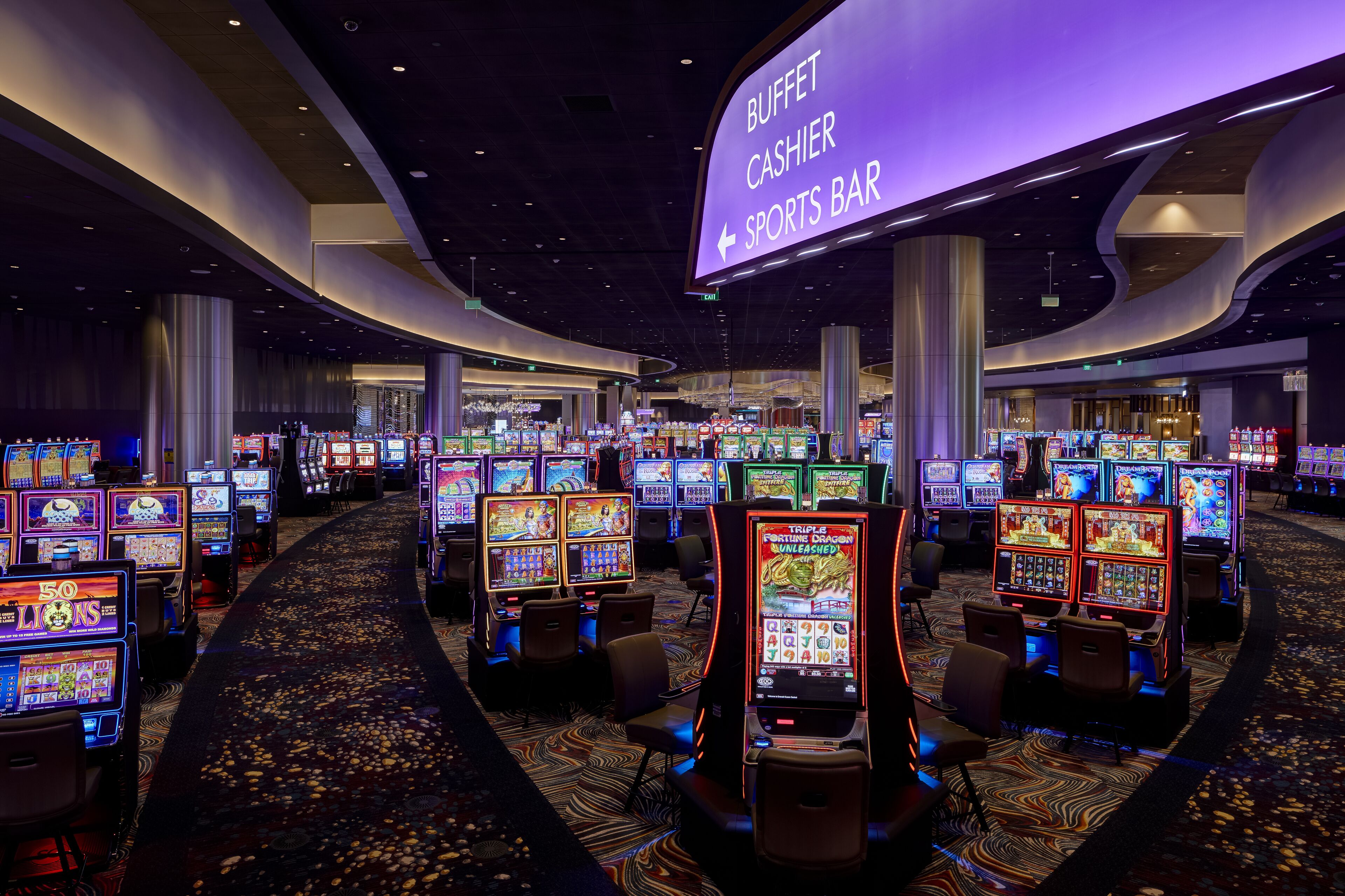 Zona de casino con múltiples máquinas tragamonedas, un bufé, una caja y un bar deportivo.