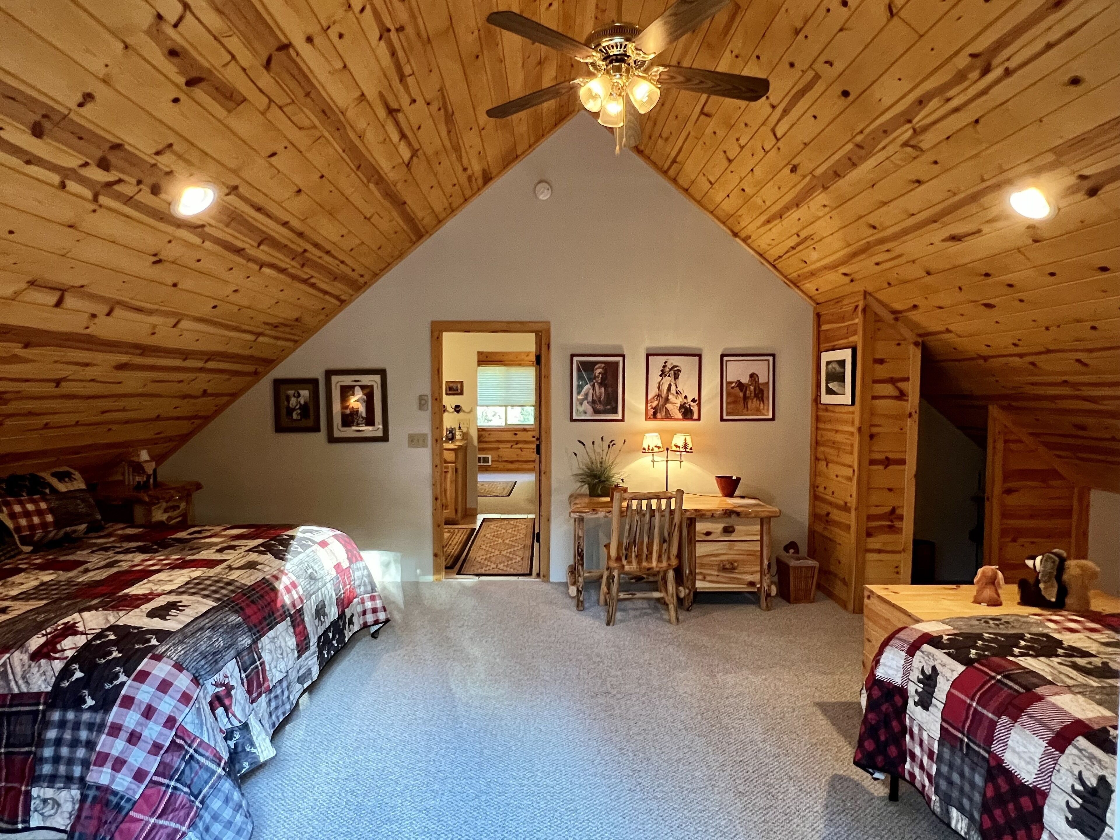 A cozy attic bedroom with two beds, a desk, and a ceiling fan.