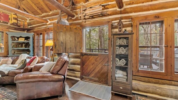 L’intérieur d’une cabane en rondins, avec un canapé en cuir, des étagères en bois et une grande fenêtre.