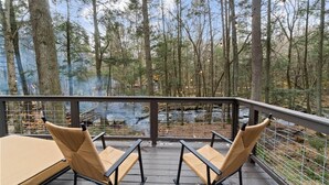 Une terrasse dotée de deux fauteuils en osier et d’une table, offrant une vue sur une forêt et un ruisseau.