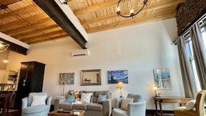 A spacious living room with a high wooden ceiling, a fireplace, and a dining area visible in the background. - Historic 1 bed 1 bath in 1920's Chevy (Mountain Home, AR, 72653)