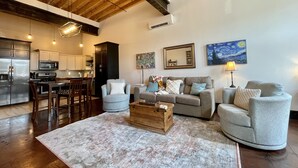 A spacious living area with a high ceiling, a kitchen in the background, and a cozy seating arrangement. - Historic 1 bed 1 bath in 1920's Chevy (Mountain Home, AR, 72653)