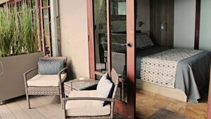 Una habitación con una cama, una silla de mimbre y una mesita.