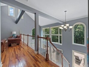 Stunning interior with a high ceiling, wooden staircase, and large window offering a view of lush greenery.