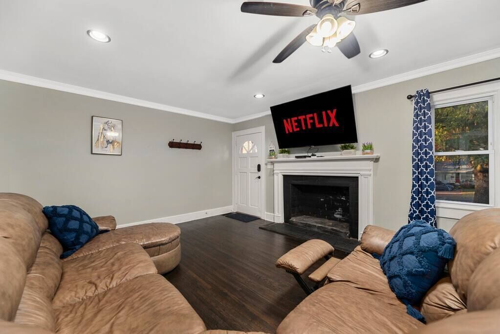 A living room with a fireplace, a ceiling fan, and a TV mounted above it.