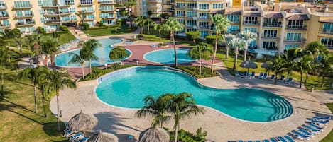 A resort with multiple swimming pools, sun loungers, and palm trees.