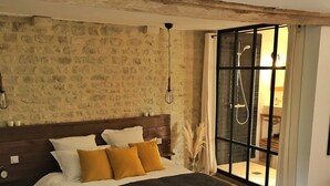 Une chambre avec un mur en pierre, un cadre de lit en bois et une grande fenêtre avec des rideaux.