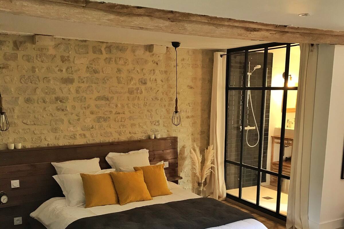 Une chambre avec un mur en pierre, un cadre de lit en bois et une grande fenêtre avec des rideaux.