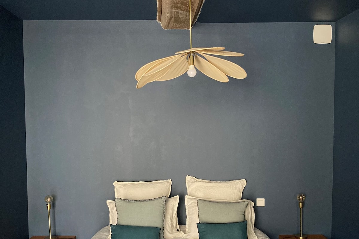 Une chambre à coucher avec un lit, deux tables de chevet, un luminaire au plafond original et un mur bleu foncé.