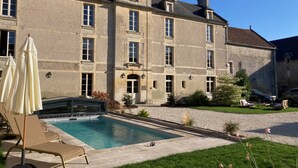 Un grand bâtiment en pierre doté d’une piscine et d’un espace extérieur aménagé pour s’asseoir.