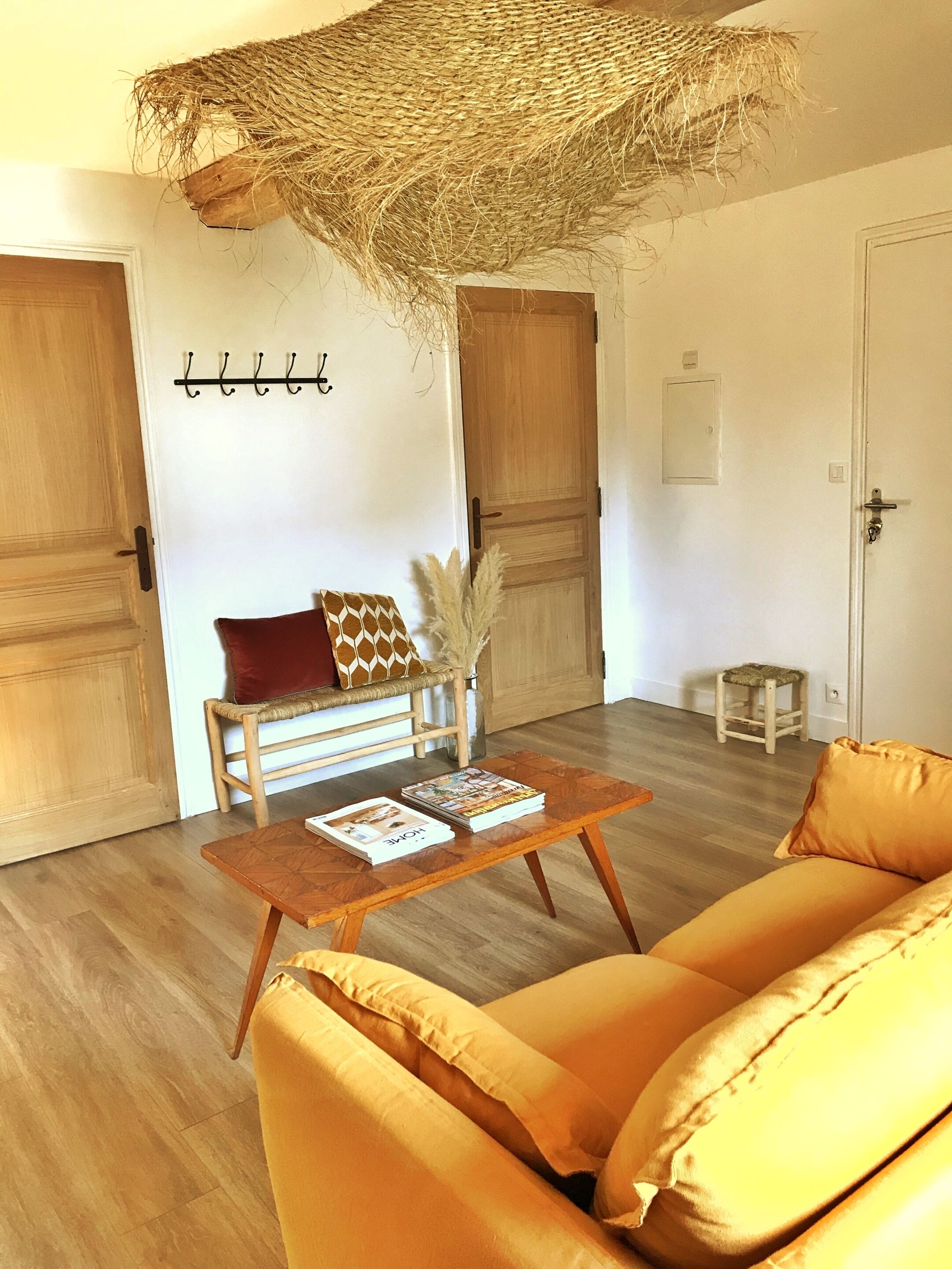 Une pièce avec un plancher en bois, un canapé, une table basse avec des magazines, un panier suspendu et une porte avec un porte-manteau.