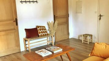 Une pièce avec un plancher en bois, un canapé, une table basse avec des magazines, un panier suspendu et une porte avec un porte-manteau.