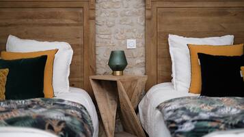 Une chambre à coucher avec deux lits, chacun agrémenté d’oreillers blancs et colorés, et une petite table de chevet en bois avec une lampe verte placée entre les deux.
