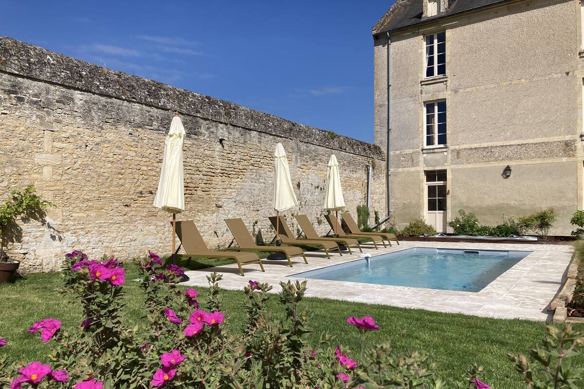 Un espace piscine agrémenté de chaises longues et de parasols, entouré d’un mur de pierre et d’un bâtiment doté d’une fenêtre.