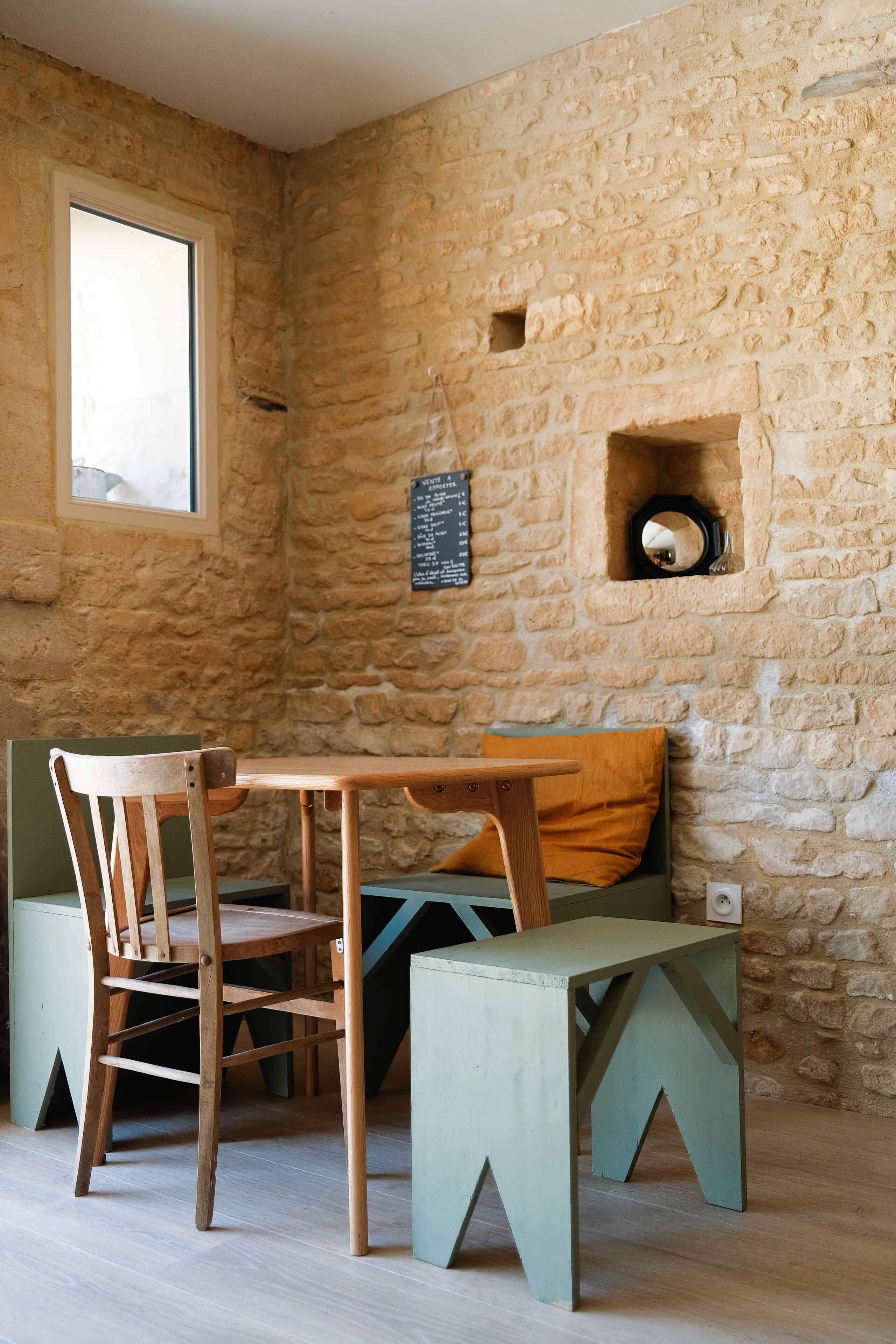 A rustic room with a stone wall, a wooden table, a green bench, and a wooden chair.