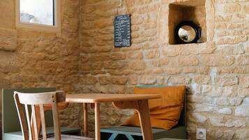 A rustic room with a stone wall, a wooden table, a green bench, and a wooden chair.