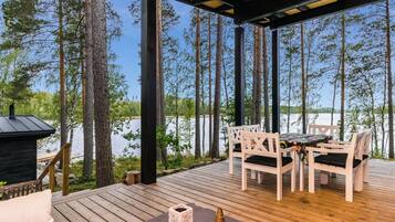 Een houten terras met een tafel en stoelen, met uitzicht op een meer met bomen.