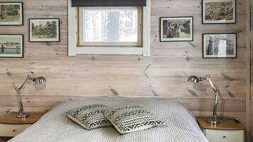 A bedroom with a bed, two bedside lamps, a window, and several framed pictures on the wall.