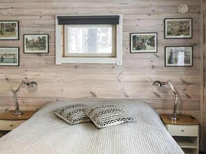 Un dormitorio con una cama, dos lámparas de noche, una ventana y varias fotografías enmarcadas en la pared.