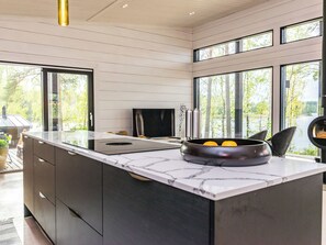 Una cocina moderna con una isla grande, un televisor de pantalla plana y vistas a un lago a través de amplios ventanales.