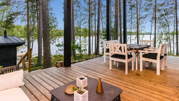 Eine Holzterrasse mit Tisch und Stühlen mit Blick auf einen See, umgeben von hohen Bäumen.