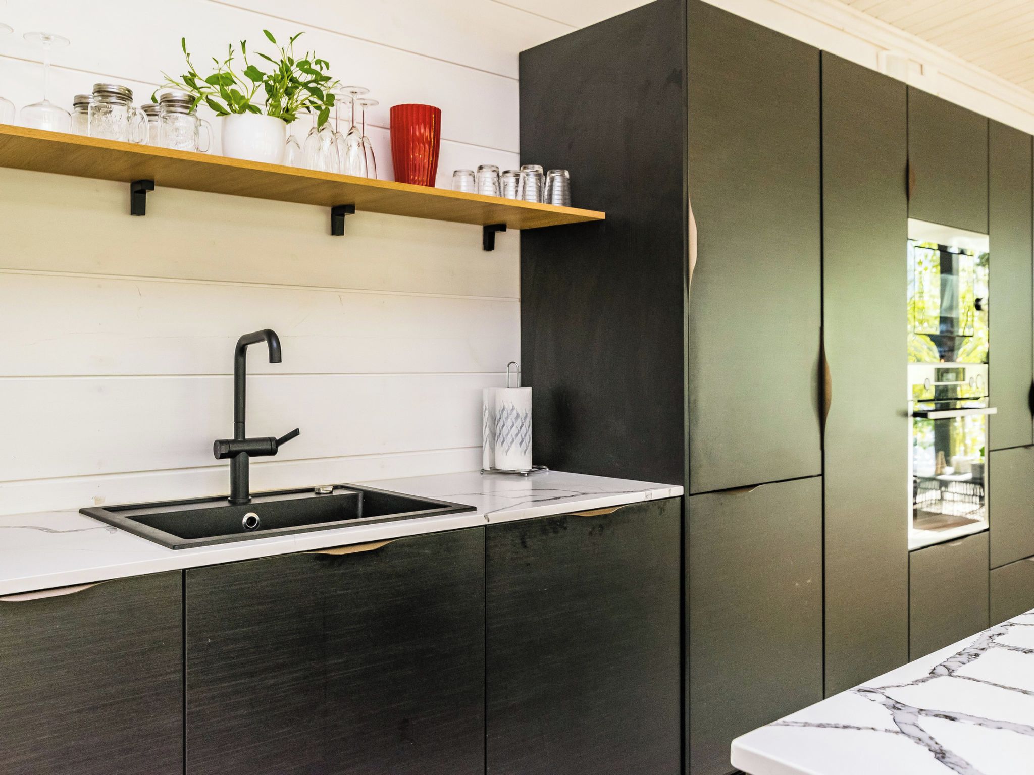Une cuisine moderne avec un évier noir, un plan de travail blanc et une étagère en bois au-dessus.