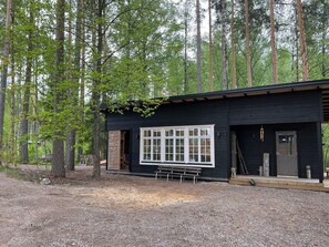 Eine Hütte mit einem großen Fenster, einer Bank davor und bewaldeter Umgebung.