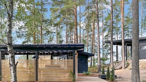 Eine moderne Holzhütte mit einer Holzterrasse, umgeben von hoch aufragenden Kiefern.