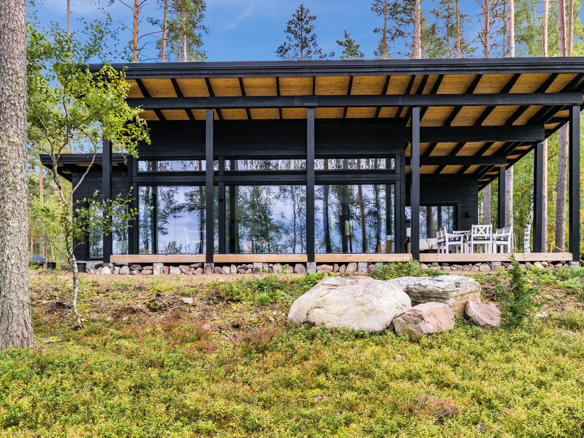 Eine moderne Holzkonstruktion mit großen Fenstern, einem Steinfundament und einer natürlichen Umgebung.