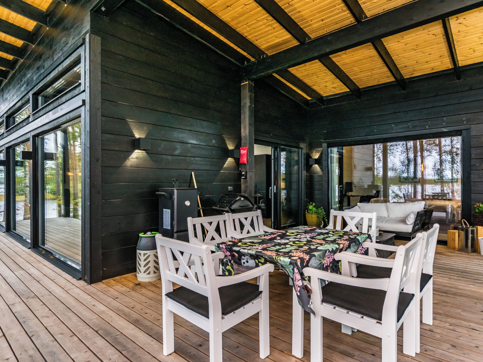 An outdoor covered patio with a dining table and chairs, a grill, and a view of the surrounding area.