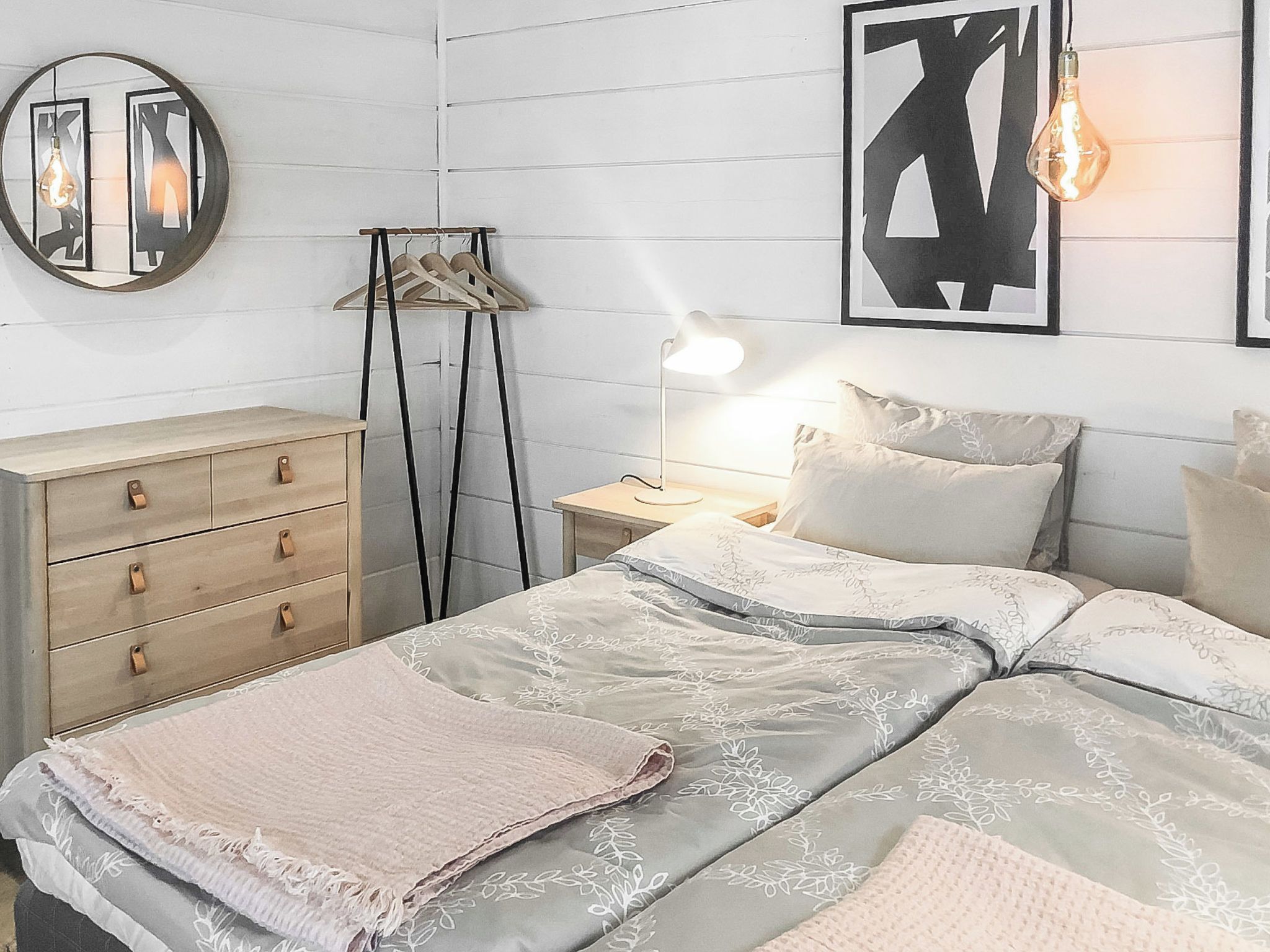 Een slaapkamer met een bed, nachtkastje, lamp, dressoir en wanddecoratie.