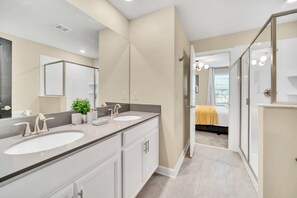 A modern bathroom with dual sinks, a large mirror, and a walk-in shower.