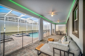 A covered outdoor area with a pool, seating, and a ceiling fan.
