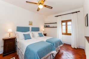 A bedroom with two beds, a ceiling fan, a window with curtains, and a wooden floor. - Villa Rinaldo by MMega (Arezzo)