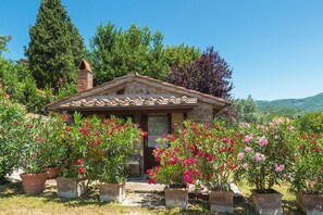 A small stone building with a tiled roof, surrounded by potted plants and flowers. - Villa Rinaldo by MMega (Arezzo)
