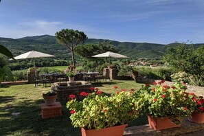 An outdoor seating area with tables and chairs, surrounded by potted plants and a view of green hills. - Villa Rinaldo by MMega (Arezzo)