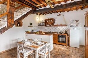 A kitchen with a wooden island, white cabinets, and a dining area with a table set for four. - Villa Rinaldo by MMega (Arezzo)
