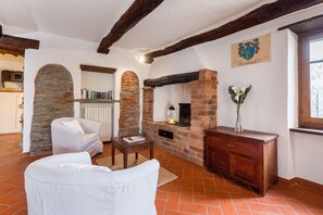 A living room with a fireplace, stone archway, white furniture, and a wooden cabinet. - Villa Rinaldo by MMega (Arezzo)