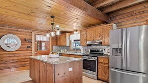 A wooden cabin kitchen with a central island, stainless steel appliances, and a hanging light fixture. - Welcome to Holly Hill – peaceful lakefront living (Denver)
