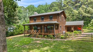 A log cabin with a porch, a small attached structure, and a sign indicating a road is not accessible. - Welcome to Holly Hill – peaceful lakefront living (Denver)