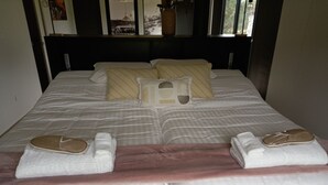 Una cama bien hecha con almohadas, una manta y dos pares de pantuflas.
