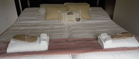 Una cama bien hecha con almohadas, una manta y dos pares de pantuflas.