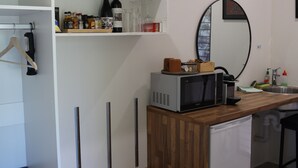 Una cocina compacta con microondas, un refrigerador pequeño y una encimera de madera. Encima de la encimera hay una repisa con botellas y vasos varios.